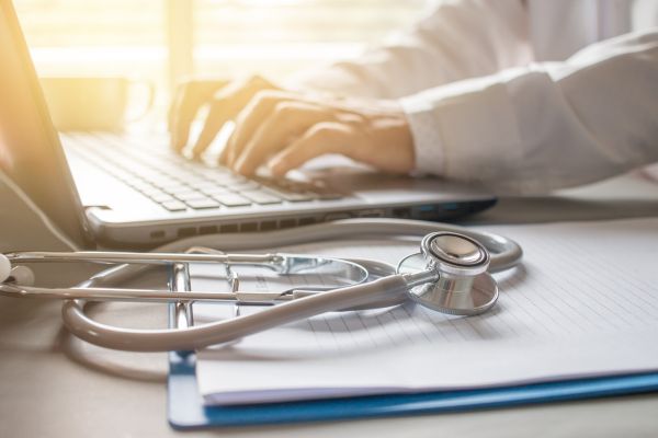 A doctor typing on the laptop with the chart on the desk